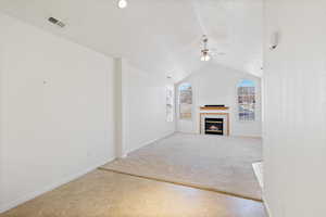 Lliving room with ceiling fan, lofted ceiling, a tile fireplace, light colored carpet, and visible vents