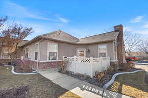 View of front facade featuring brick siding, fence, stucco siding, a chimney, and a front yard