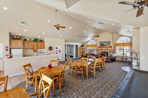 Dining space with high vaulted ceiling, a glass covered fireplace, visible vents, and a ceiling fan