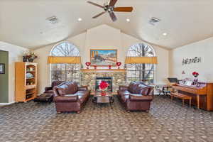 Living room featuring a fireplace, visible vents, dark carpet, and a ceiling fan