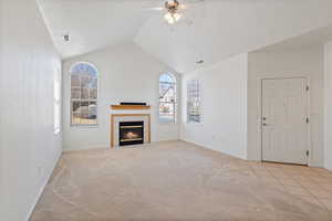 Unfurnished living room featuring visible vents, a ceiling fan, light colored carpet, lofted ceiling, and a fireplace