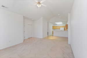 Living room with light carpe, baseboards, ceiling fan, and vaulted ceiling