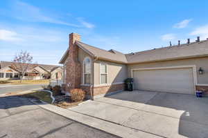 View of north side of property with concrete driveway, brick siding, a chimney, and stucco siding