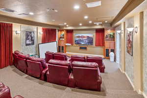 Home theater featuring recessed lighting, light colored carpet, visible vents, ornamental molding, and a textured ceiling