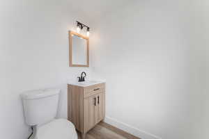 Bathroom featuring toilet, baseboards, wood finished floors, and vanity