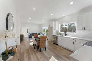 Kitchen with light wood finished floors, decorative backsplash, white cabinets, a sink, and dishwasher