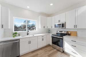 Kitchen with stainless steel appliances, backsplash, white cabinetry, a sink, and light wood-type flooring