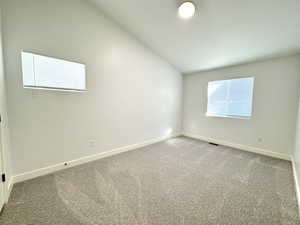 Empty room featuring carpet floors, visible vents, vaulted ceiling, and baseboards