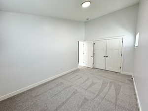 Unfurnished bedroom featuring light carpet, high vaulted ceiling, a closet, and baseboards