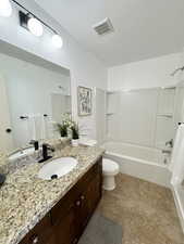 Full bathroom with a textured ceiling, toilet, vanity, visible vents, and  shower combination