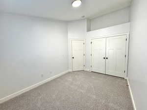 Unfurnished bedroom featuring a closet, light colored carpet, vaulted ceiling, and baseboards