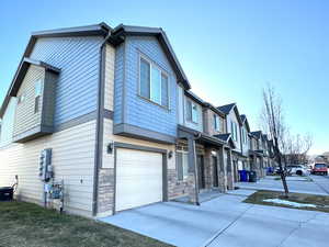 View of front of house with driveway, stone siding, a residential view, an attached garage, and a front lawn