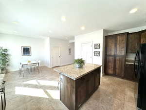 Kitchen featuring light stone counters, dark brown cabinetry, a kitchen island, baseboards, and freestanding refrigerator