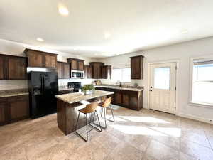 Kitchen with dark brown cabinetry, a kitchen island, a kitchen breakfast bar, light stone countertops, and black appliances