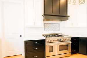 Kitchen with backsplash, ventilation hood, range with two ovens, and light countertops