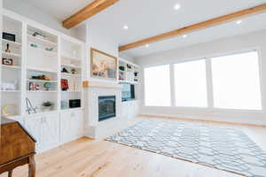 Living area featuring light wood-type flooring, beamed ceiling, a brick fireplace, and recessed lighting.