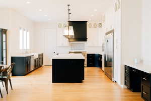 Kitchen featuring light countertops, hanging light fixtures, a kitchen island, and wall chimney range hood