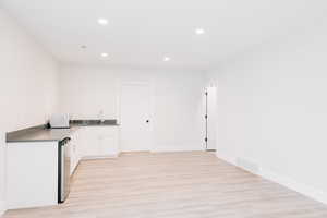 Kitchenette featuring microwave, a sink, light wood-style floors, and white cabinets