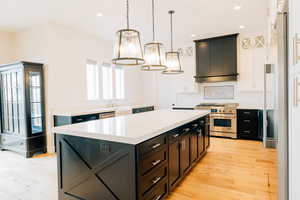 Kitchen with decorative light fixtures, custom range hood, light countertops, and a kitchen island.