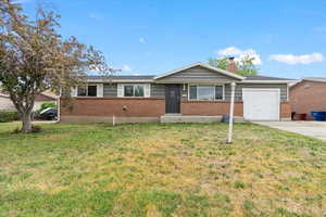 Ranch-style home with a garage, driveway, a front lawn, a chimney, and brick siding
