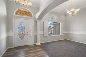 Entryway featuring ornate columns, plenty of natural light, dark wood-type flooring, and a notable chandelier