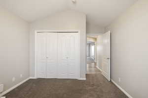 Unfurnished bedroom featuring vaulted ceiling, dark carpet, and a closet