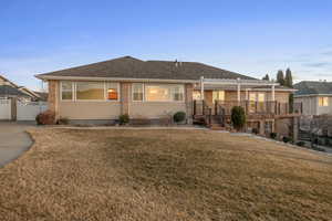 Ranch-style home featuring a wooden deck, a pergola, and a front lawn