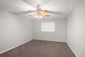 Empty room featuring ceiling fan, dark carpet, and a textured ceiling