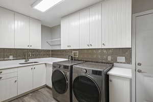 Laundry room with washer and dryer, sink, light hardwood / wood-style flooring, and cabinets