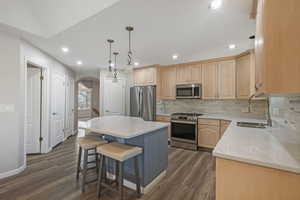 Kitchen with light brown cabinetry, sink, stainless steel appliances, and a center island