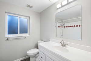 Bathroom with vanity, a tile shower, and toilet