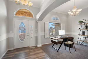 Entrance foyer featuring dark hardwood / wood-style flooring, a notable chandelier, ornamental molding, and decorative columns