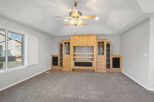 Unfurnished living room with ceiling fan, vaulted ceiling, and dark colored carpet