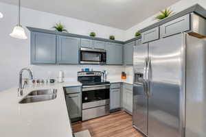 Kitchen featuring light wood finished floors, stainless steel appliances, light countertops, pendant lighting, and a sink