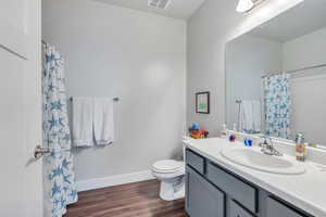 Bathroom with visible vents, toilet, vanity, wood finished floors, and baseboards