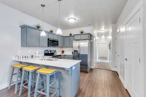 Kitchen featuring a breakfast bar area, gray cabinets, light countertops, appliances with stainless steel finishes, and a peninsula