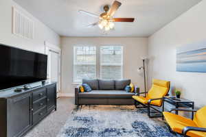 Living room featuring light carpet, baseboards, visible vents, a ceiling fan, and a textured ceiling