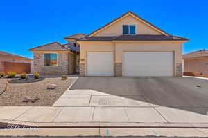 View of front of house with driveway, a garage, stone siding, fence, and stucco siding