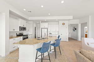 Kitchen with backsplash, appliances with stainless steel finishes, white cabinets, a sink, and a kitchen bar