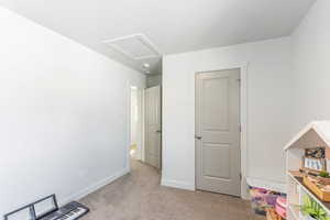 Unfurnished bedroom with attic access, baseboards, and light colored carpet