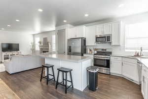 Kitchen with a breakfast bar, dark wood-type flooring, stainless steel appliances, white cabinetry, and a sink