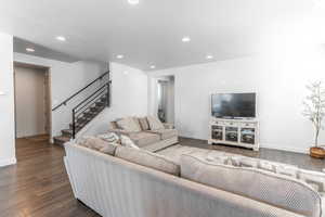 Living room featuring dark wood-style floors, stairs, baseboards, and recessed lighting