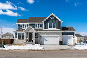 Craftsman-style house with concrete driveway, stone siding, an attached garage, fence, and board and batten siding