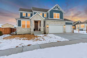 Craftsman-style home with a garage, concrete driveway, stone siding, fence, and board and batten siding