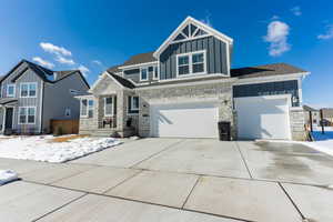 View of front of home with an attached garage, driveway, board and batten siding, and stone siding