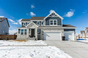 Craftsman-style home with driveway, stone siding, an attached garage, fence, and board and batten siding