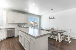 Kitchen featuring dark wood-style floors, white cabinetry, backsplash, dishwasher, and decorative light fixtures