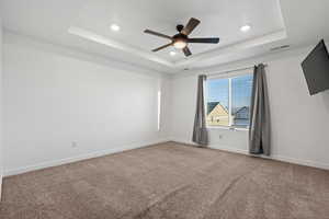 Empty room with a tray ceiling, visible vents, and baseboards