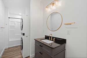 Bathroom featuring baseboards, wood finished floors, stacked washer / drying machine,  shower combination, and vanity