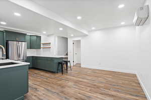 Kitchen featuring a breakfast bar, a wall mounted AC, freestanding refrigerator, open shelves, and green cabinetry